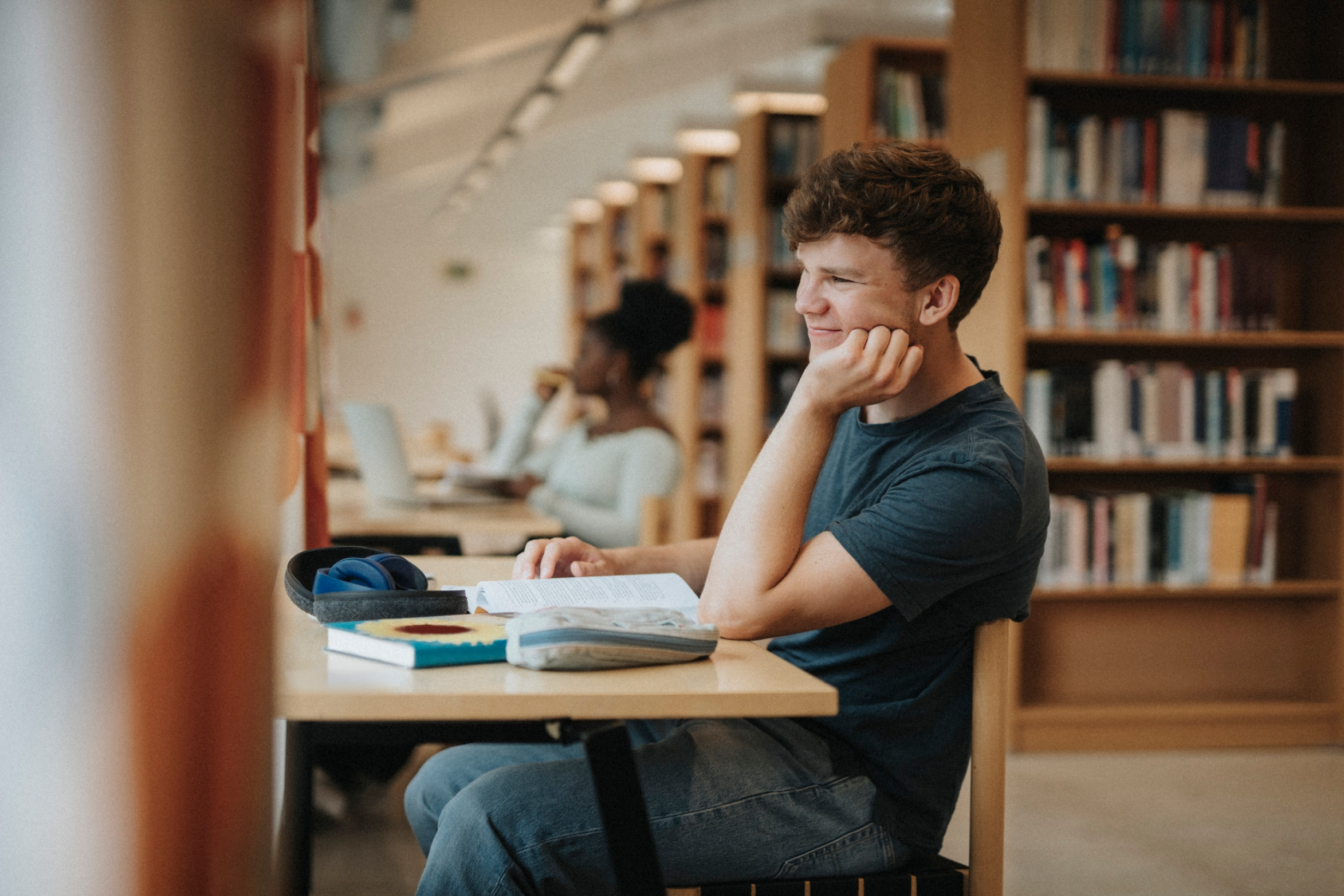 Un étudiant qui étudie à un bureau avec des livres et un ordinateur portable dans une bibliothèque.