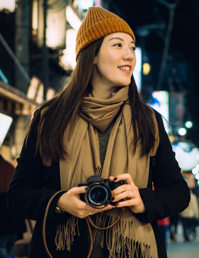 Une jeune femme portant un chapeau tient un appareil photo la nuit