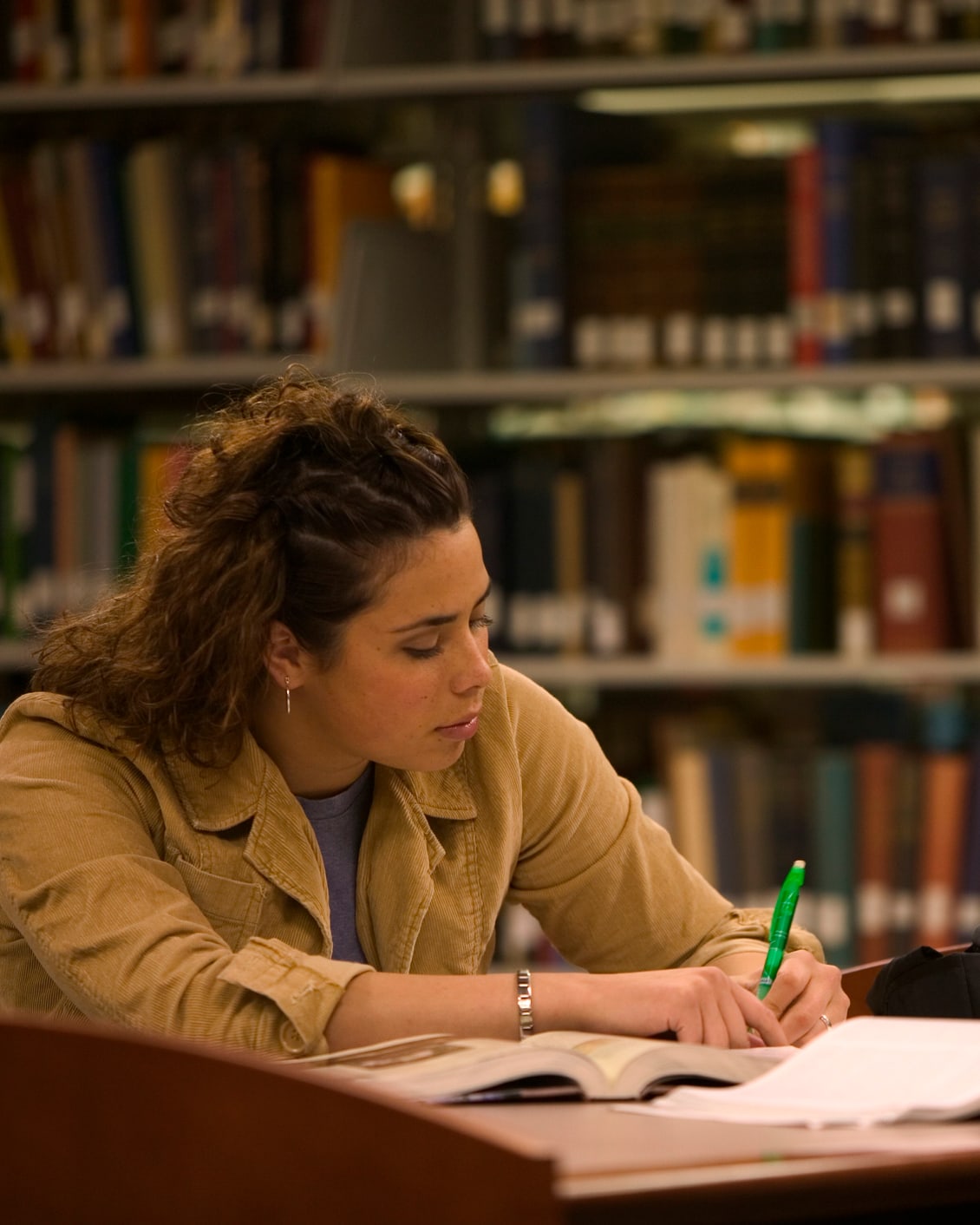 Jeune femme à la bibliothèque écrit dans un livre avec un stylo vert.