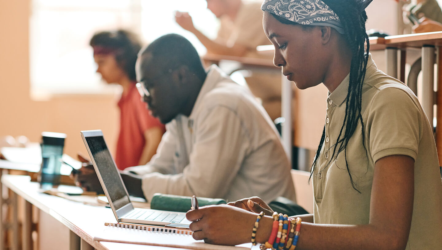Des élèves travaillant en classe, avec un élève utilisant un ordinateur portable et prenant des notes à un bureau.